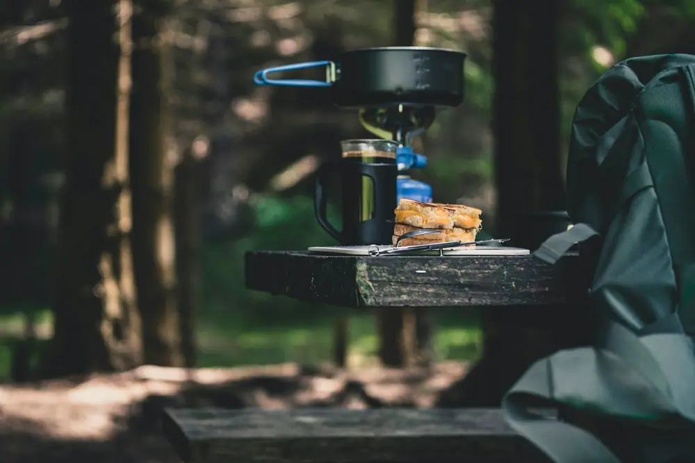 Small gas camping stove with a pot set up on a wooden camp table in the woods