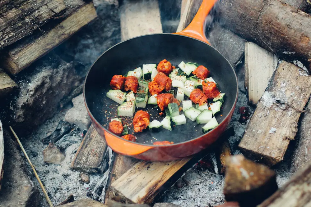 Diced tomatoes, zucchini and peppers cooking in an orange skillet over campfire embers