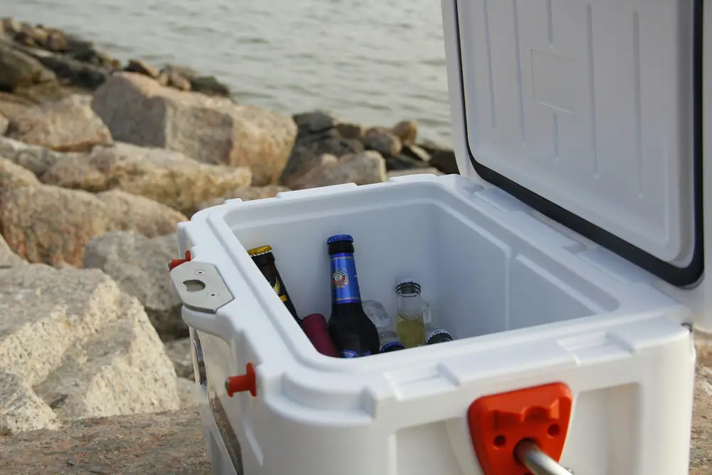Open white cooler with bottles and ice sitting on rocks beside a lake