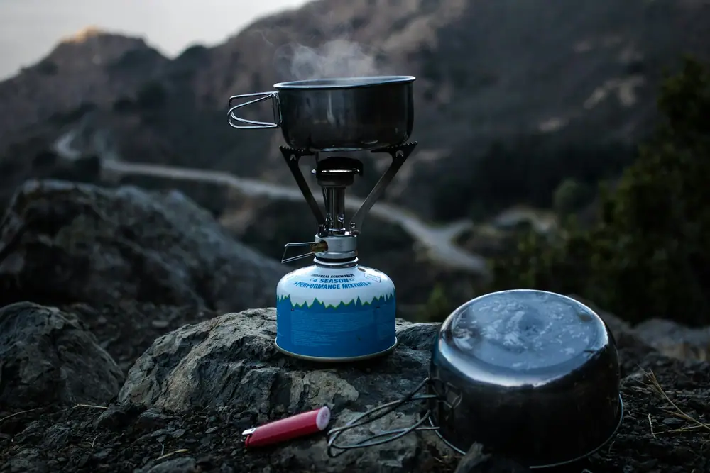 Compact gas stove with a small pot set on a rock with mountains in the background