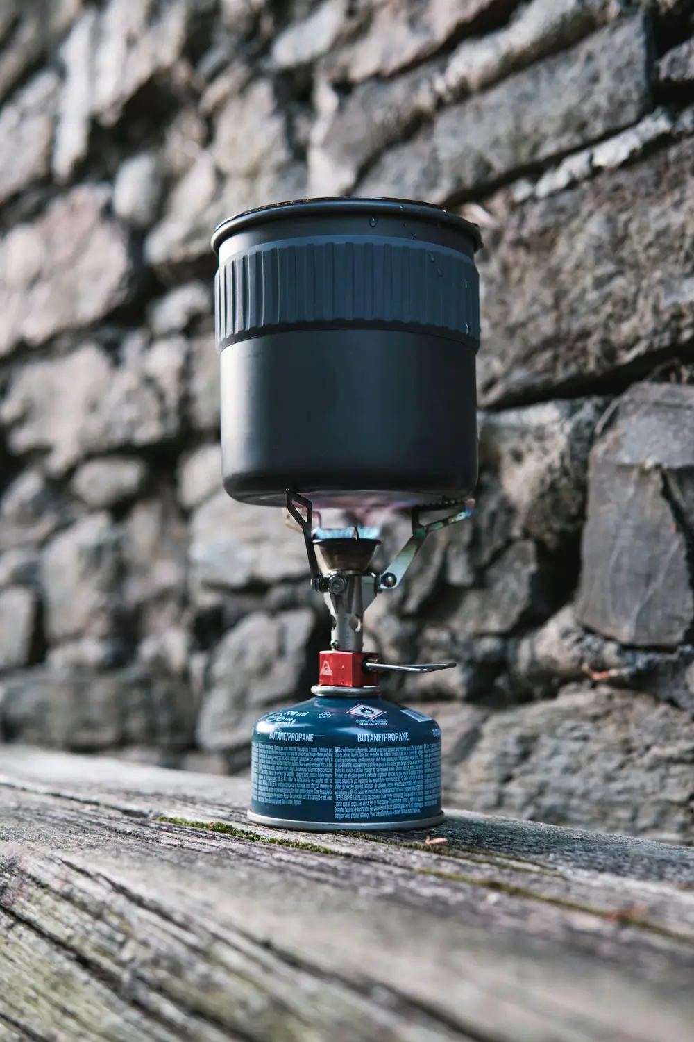 Stovetop coffee maker heating on a small camping stove on a stone wall