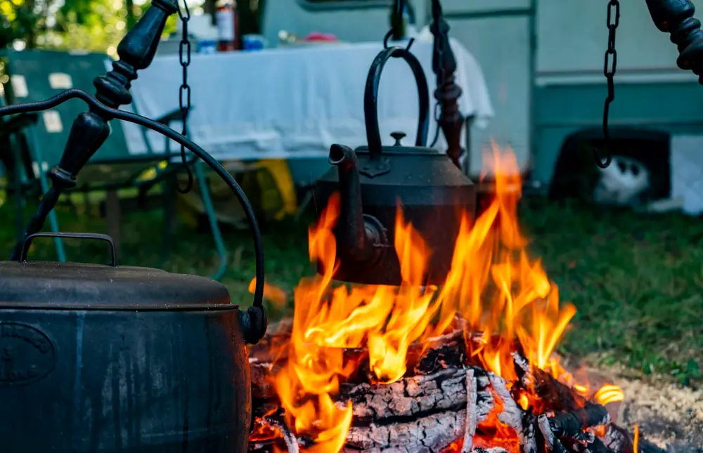Cast iron pots and a kettle hanging over a bright campfire at a campsite